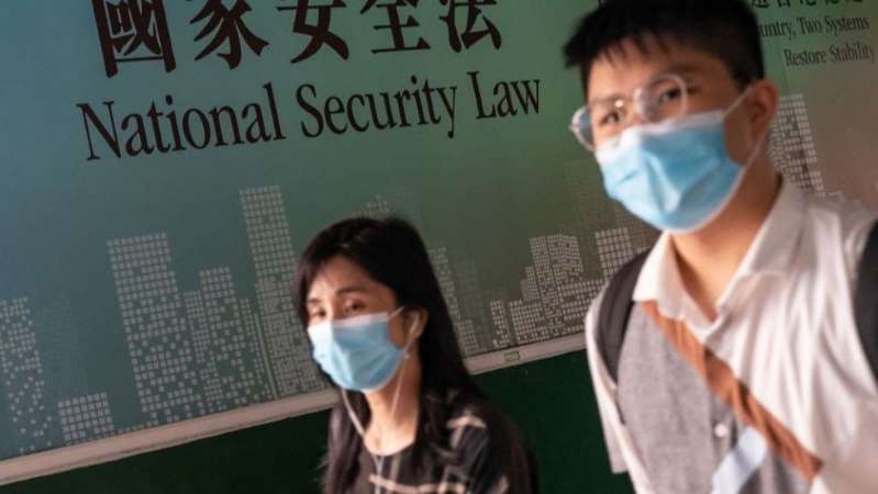 A man and a woman wearing masks with a sign behind them reading "National Security Law", referring to recently-passed Chinese National Security Law impacting Hong Kong's liberties.