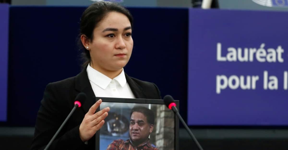 A young Uyghur woman holds up a framed photograph of her father who is imprisoned.